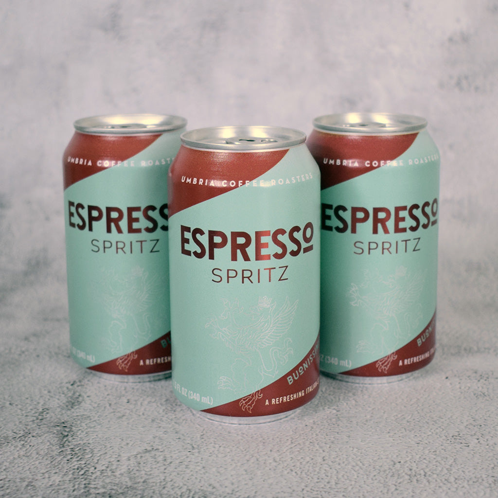 Three cans of Espresso Spritz on a textured gray surface